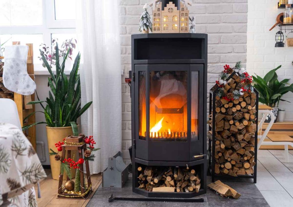 Poêle à granulé moderne en fonte noire allumé dans un salon, avec des bûches de bois empilées à côté, créant une ambiance chaleureuse. Pensez à l'entretien de votre appareil avec une Bougie résistance d'allumage céramique pour poêle à granulé.